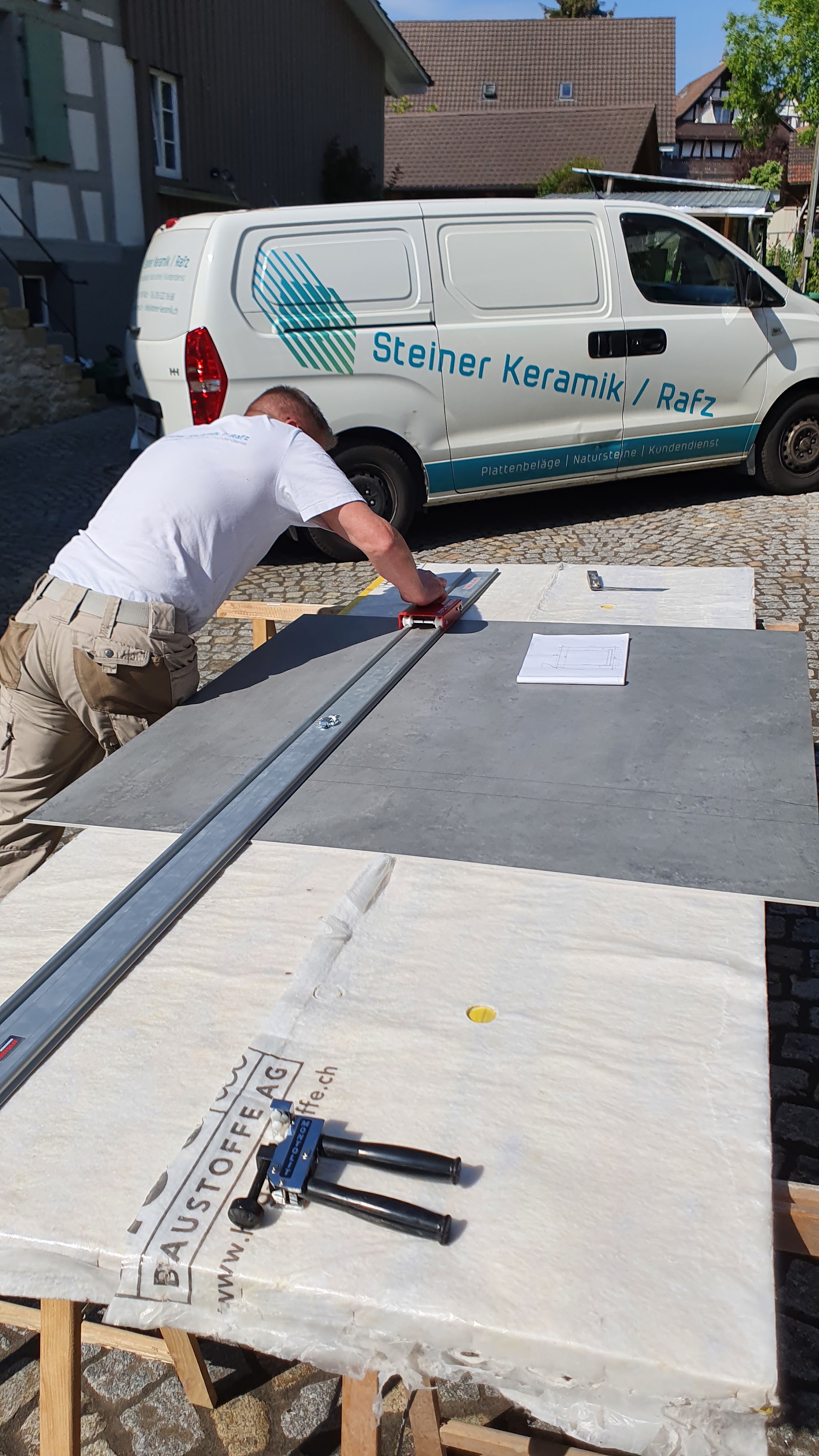 Plattenleger beim Verlegen einer Grossformatplatte vor dem Firmenbus